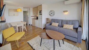 A modern living room with a grey sofa, yellow chairs, a wooden coffee table, and a kitchen in the background. - Upstays Terrace Pool Parking 40m² Apartment (Cannes)