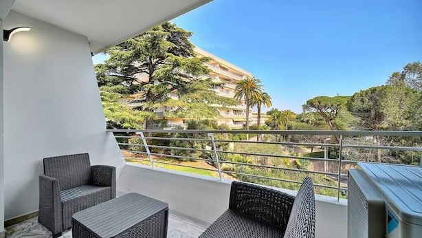 Un balcon avec des meubles en osier, une vue sur un immeuble et un palmier.