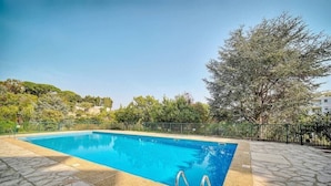 Une piscine rectangulaire à l’eau d’un bleu limpide, entourée de carreaux de pierre et d’une clôture en métal.