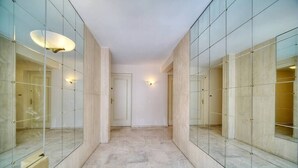 Un couloir aux murs recouverts de miroirs et au sol en marbre, qui mène à une porte.