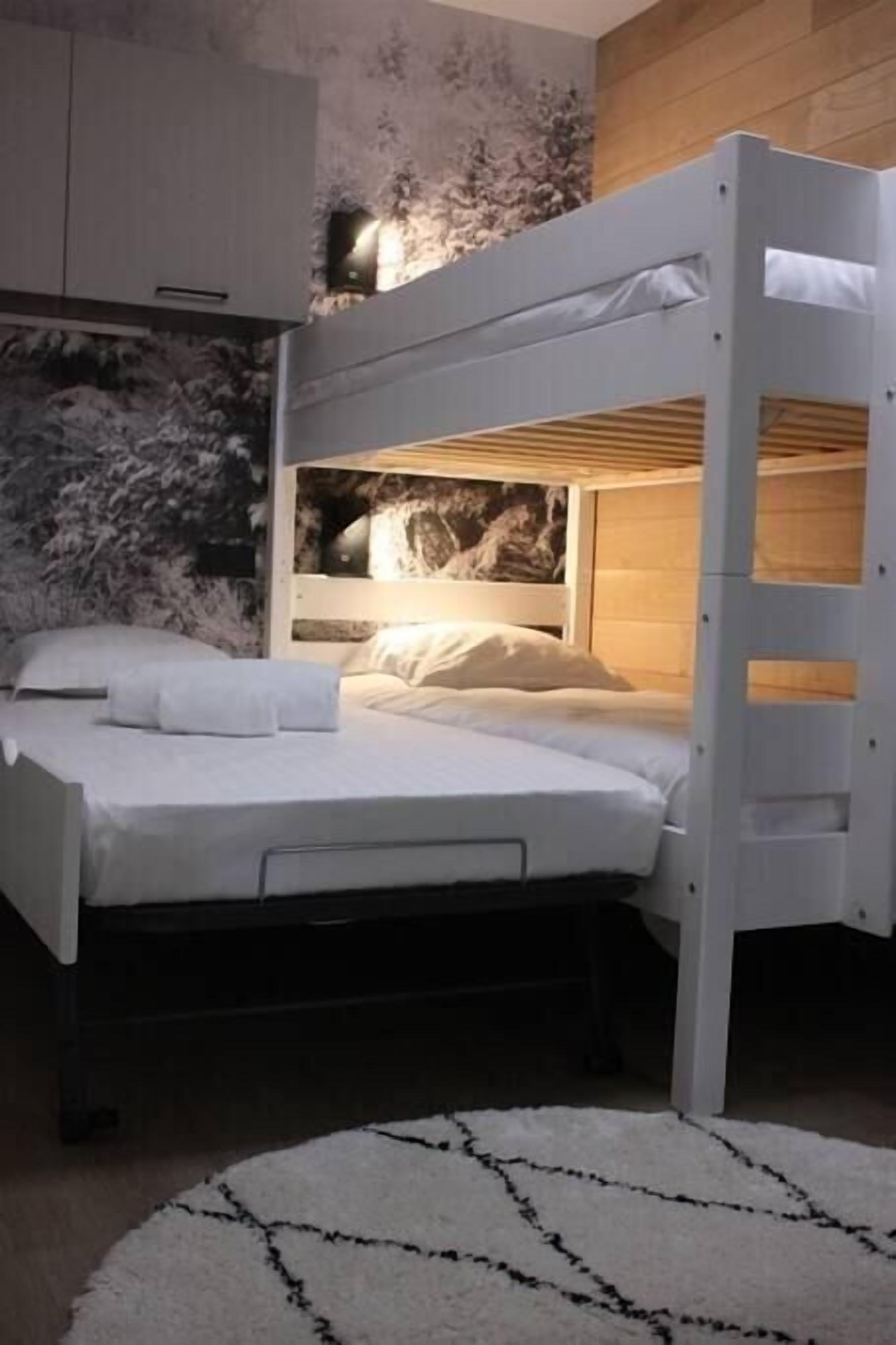 Ein Stockbett mit weißer Matratze und Kissen, einem Holzkopfstück und einer Wandmalerei.