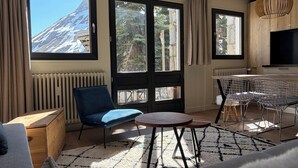 A modern room with a large window, a blue chair, a round table, and a TV. - Upstays Cosy Family Ski Near Slopes and Lake (Tignes)