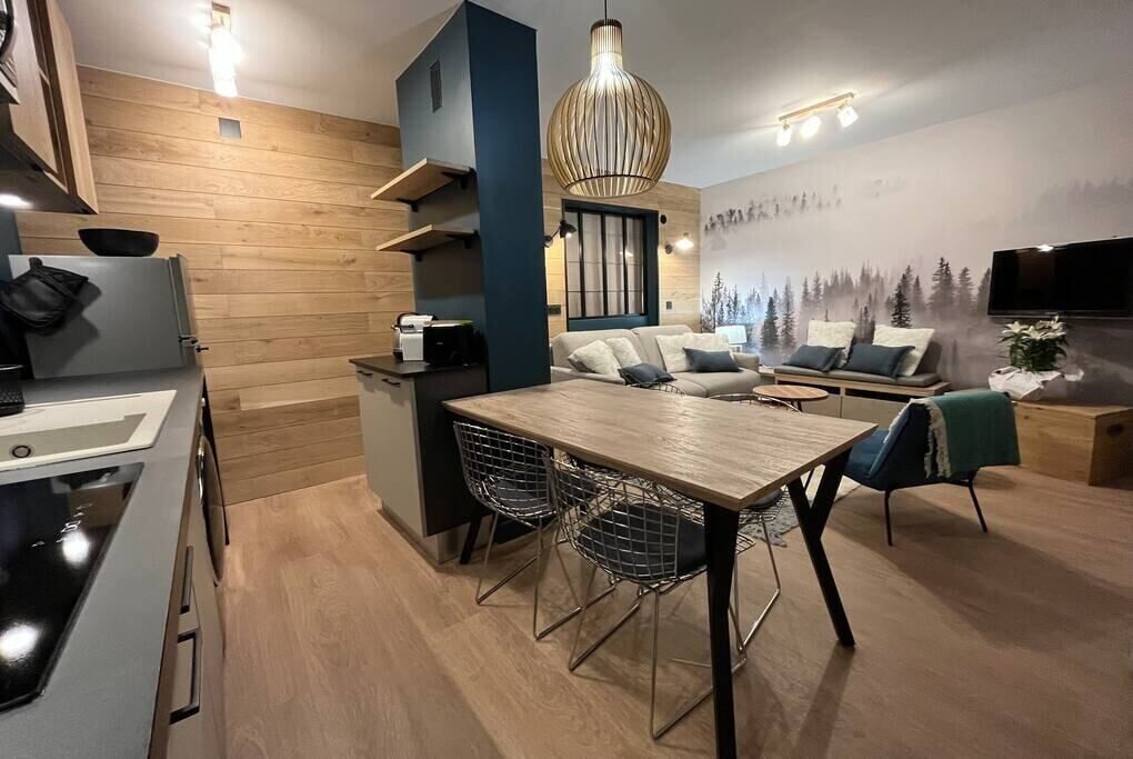A modern kitchen with a dining area, wooden walls, and a large pendant light.