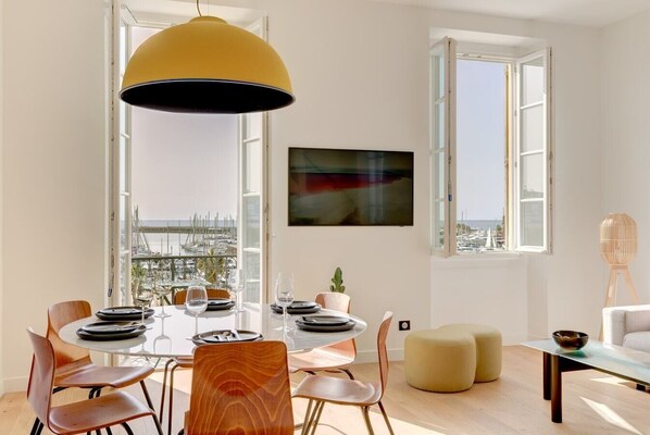 A dining area with a table set for four, large windows, and a view of the marina. - UPSTAYS Harbor Balcony 85m² Apartment Palais (Cannes)