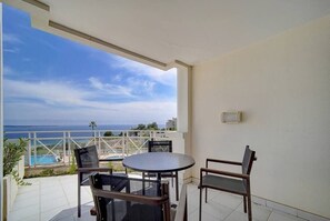A balcony with a table and chairs, overlooking a pool and the sea.