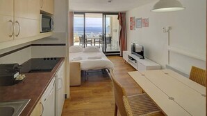 Kompakti hotellihuone, jossa on pieni keittiönurkkaus, sänky, televisio ja parveke, jolta on näkymä.