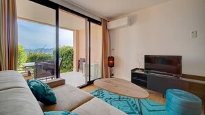 A modern living room with a sofa, a coffee table, a TV, and a sliding glass door leading to an outdoor area.