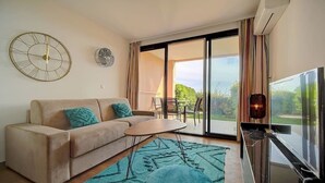 A living room with a sofa, a coffee table, a TV, and a sliding glass door leading to an outdoor area.