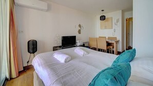 A hotel room with a bed, a desk, a chair, a television, and an air conditioning unit.