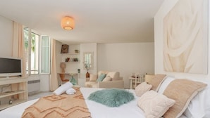 A modern hotel room with a large bed, a TV, a sofa, and a dining area. - Upstays Palais Center 38m² Studio (Cannes)