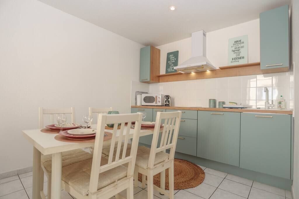 A compact kitchen with teal cabinets, a white countertop, and a dining area with white chairs.