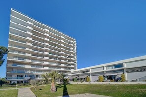 Un hotel de varios pisos con diseño moderno, que cuenta con balcones en cada planta, un patio central con palmeras y un área exterior cubierta.