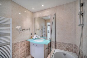 Un bany amb banyera, un espai de dutxa amb portes de vidre, un lavabo amb mirall i un suport per a tovalloles.