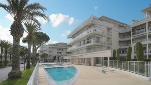 A modern multi-story building with a swimming pool, palm trees, and a well-maintained outdoor area. - Upstays Sea View 50m² Apartment Bocca (Cannes)