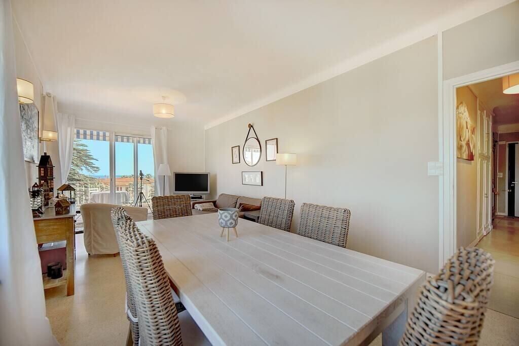 A spacious dining area with a large table and wicker chairs, a television, and framed artwork on the wall.