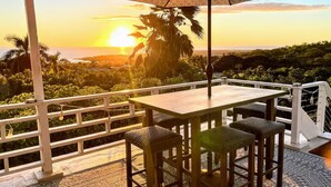 A terrace with a table and chairs, overlooking a scenic view of the sunset and palm trees. - Roof deck views, hot tub, big kitchen, 3200sf, BBQ (Kailua-Kona)