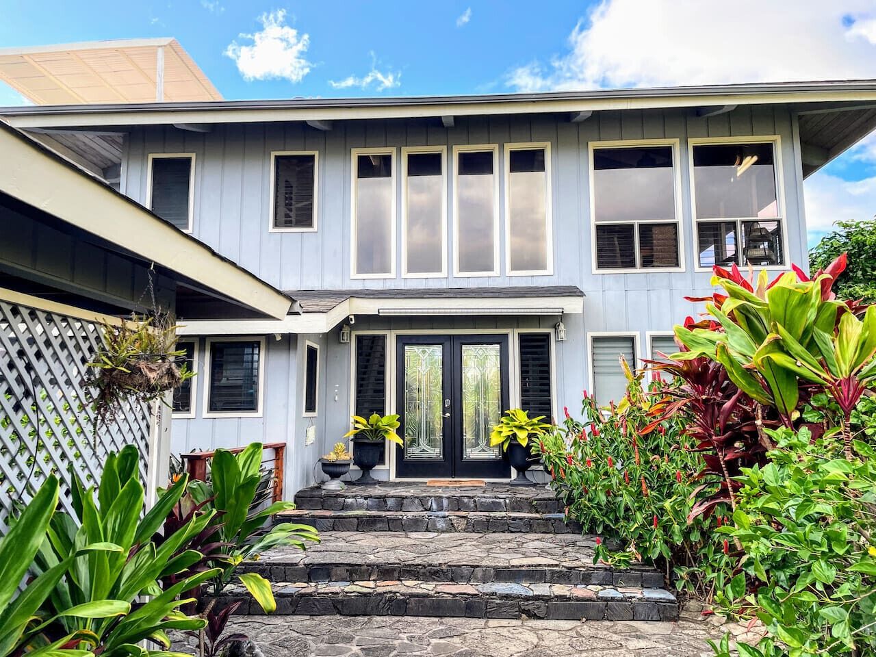A two-story house with a front porch, stone steps, and potted plants.
