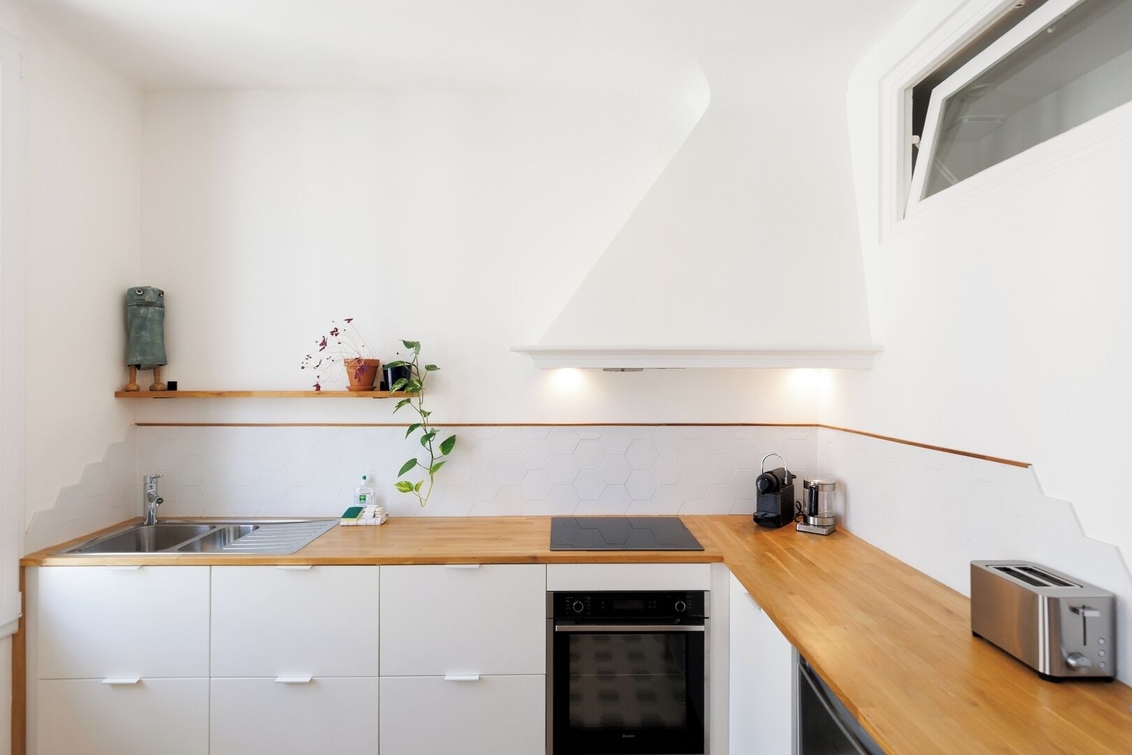 Una cocina moderna con encimera de madera, horno empotrado, lavavajillas y una ventana sobre el fregadero.