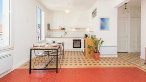 A compact kitchen with a dining area, a potted plant, and a patterned floor. - Upstays République 67m² Apartment (Cannes)