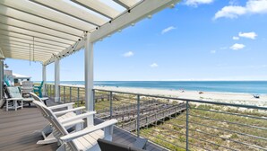 A covered deck with lounge chairs overlooking a beach.