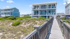 A beachfront property with a wooden boardwalk leading to a multi-story building with balconies.