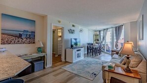 A spacious living area with a dining table, a sofa, a TV, and a kitchen area. - Ocean's Edge Retreat - St. Regis Condo #1109 (North Topsail Beach)