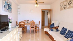 Un salon comprenant un canapé, un téléviseur, une table à manger avec des chaises et un ventilateur de plafond.
