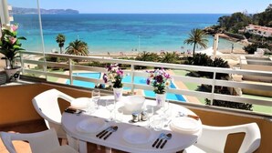 Une table à manger dressée pour quatre personnes, avec vue sur la mer et une piscine.