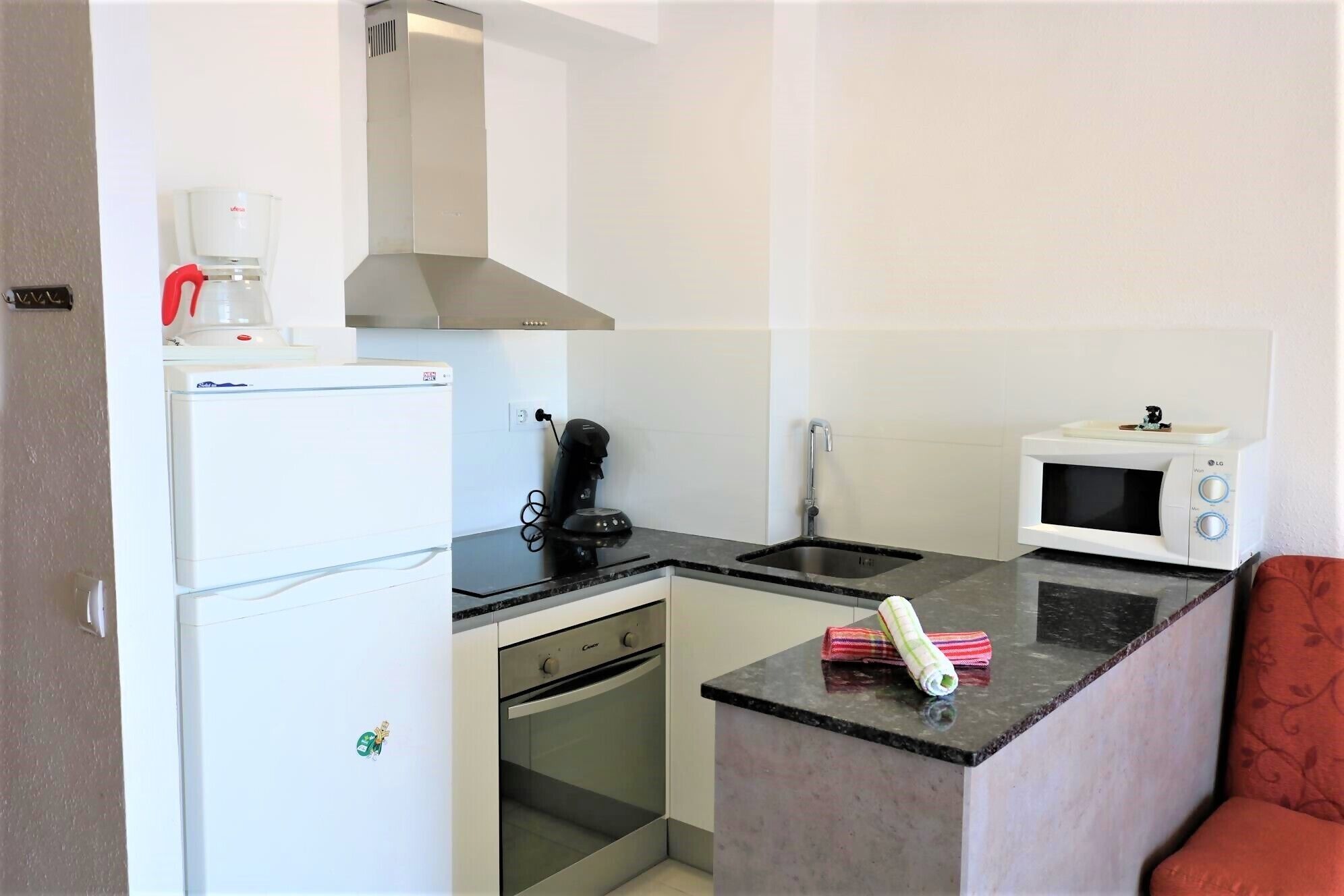 A compact kitchen with a refrigerator, stove, microwave, and a coffee maker.