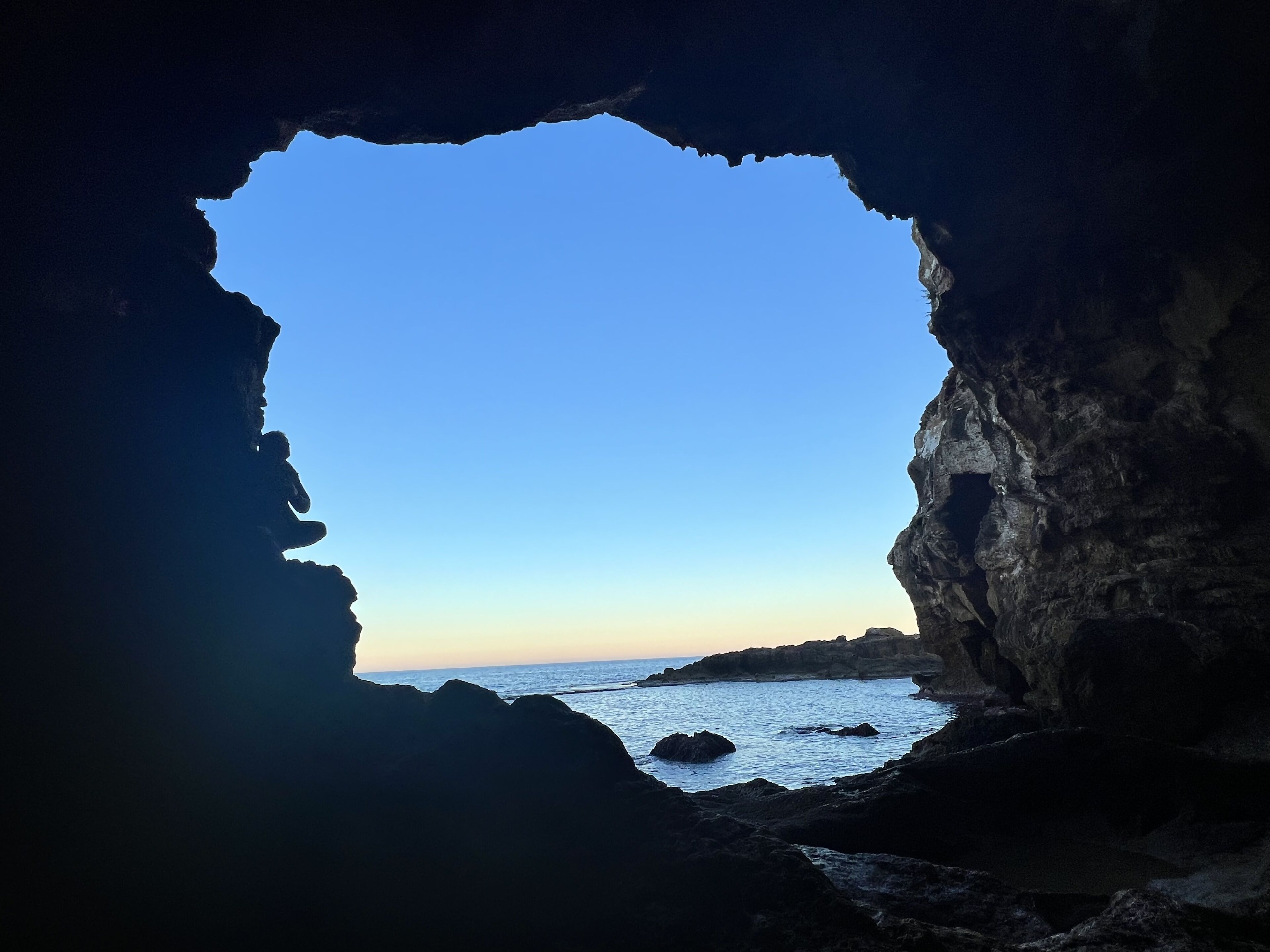 A cave opening to a coastal view with clear sky.