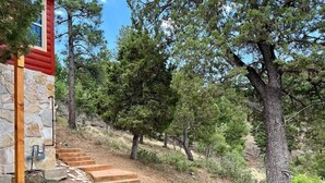 A stone building with a red exterior, a staircase leading up a hill, and a forested area. - Secluded Mountain Cabin: Hot Tub & Spectacular (Ruidoso)
