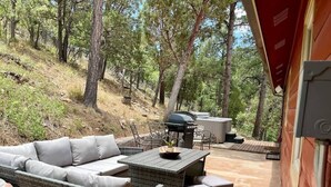 An outdoor patio with wicker furniture, a grill, and a red awning. - Secluded Mountain Cabin: Hot Tub & Spectacular (Ruidoso)
