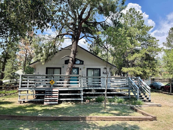 A white cabin with a porch, a staircase, and a tree in front.