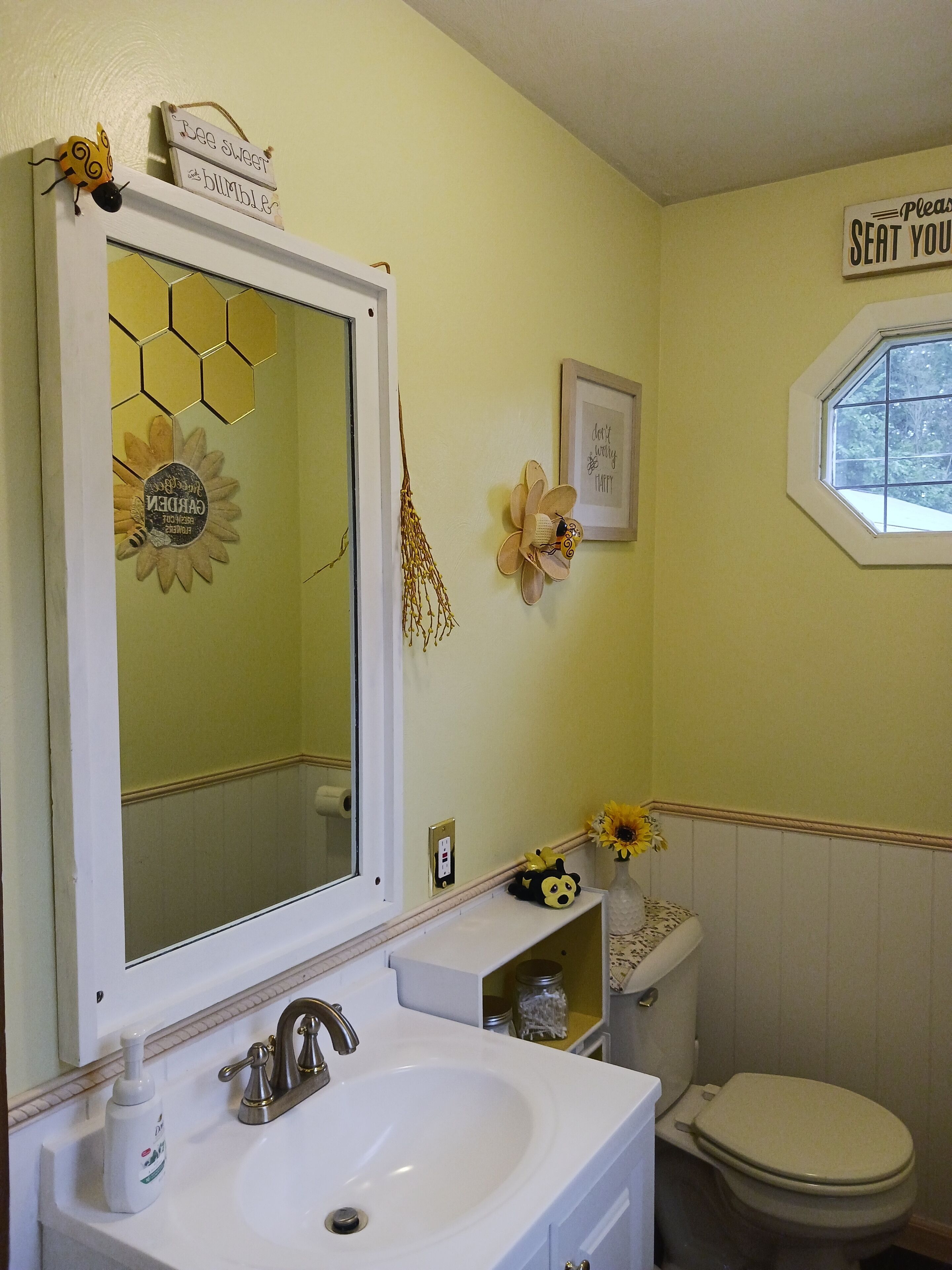 Un baño con lavamanos, espejo, inodoro y elementos decorativos como una abeja y un girasol.