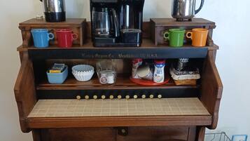 A wooden kitchenette with a coffee maker, kettle, and various mugs and containers.