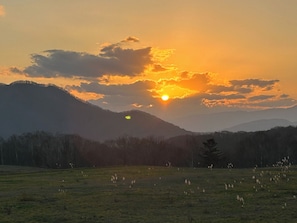 Un coucher de soleil sur un paysage montagneux, avec un champ au premier plan.