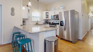 Une cuisine moderne dotée d’un îlot central, d’appareils électroménagers en acier inoxydable et de tabourets de bar de couleur turquoise.
