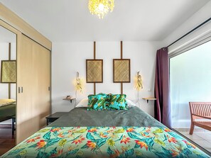 A modern bedroom with a bed, a wardrobe, a nightstand, wall art, and a large window.