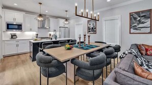 Una cocina moderna con gabinetes blancos, una isla central y un área de comedor con sillas grises.
