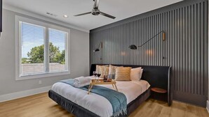 Un dormitorio moderno con una cama grande, un ventilador de techo, una ventana con persianas y una lámpara de pared.