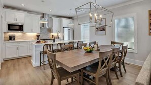 Una cocina moderna con armarios blancos, una isla central y una zona de comedor con sillas de madera.