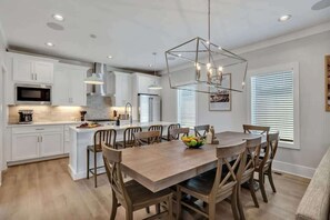 A modern kitchen with white cabinets, a central island, and a dining area with wooden chairs.