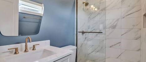 Un baño con lavamanos blanco, inodoro y ducha con mampara de vidrio.