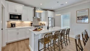 Una cocina moderna con armarios blancos, electrodomésticos de acero inoxidable y una isla central con taburetes de bar.