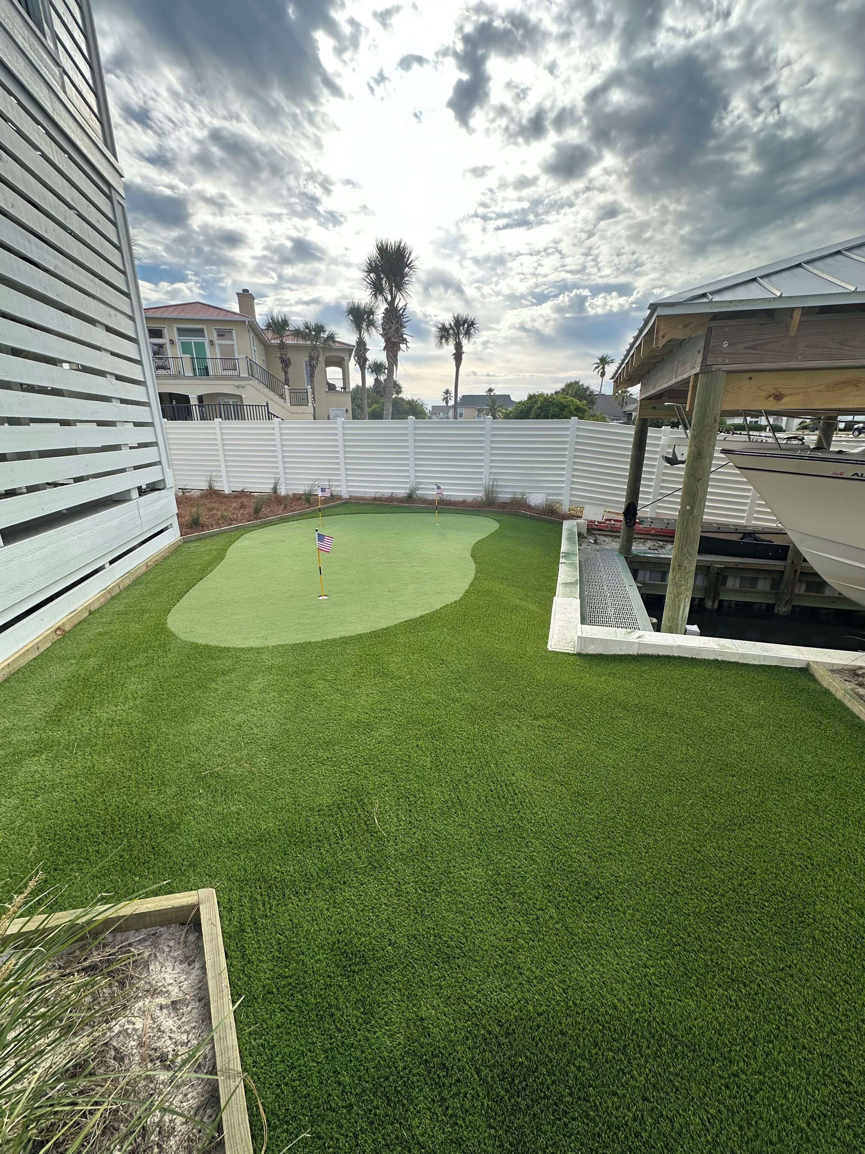 Un jardin avec une pelouse artificielle, une terrasse en bois et une clôture blanche.