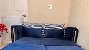 Een bed met een gewatteerd hoofdeinde en voeteinde, een thermostaat aan de muur, en een potplant.