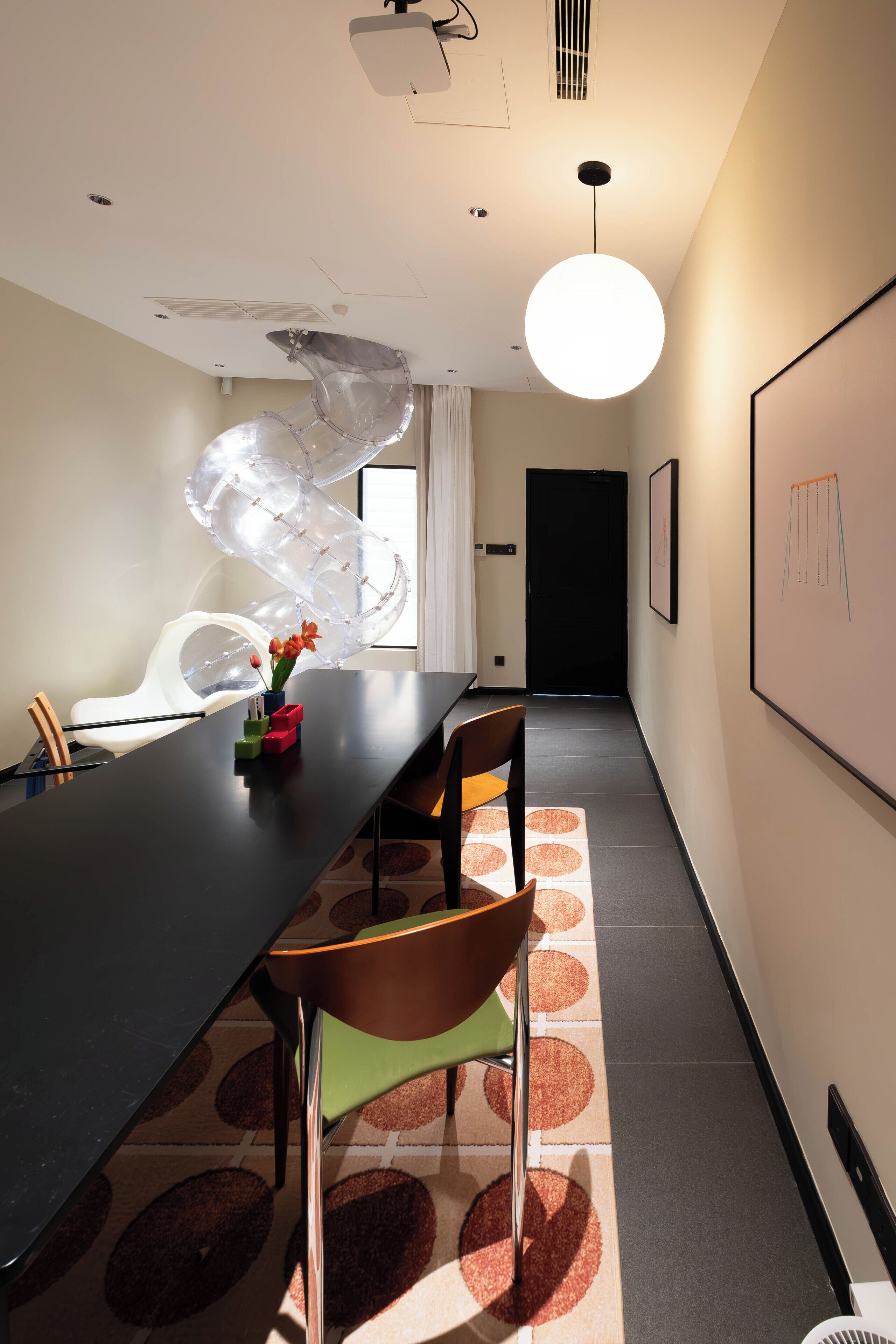 A conference room with a long table, chairs, a modern light fixture, and a whiteboard on the wall.