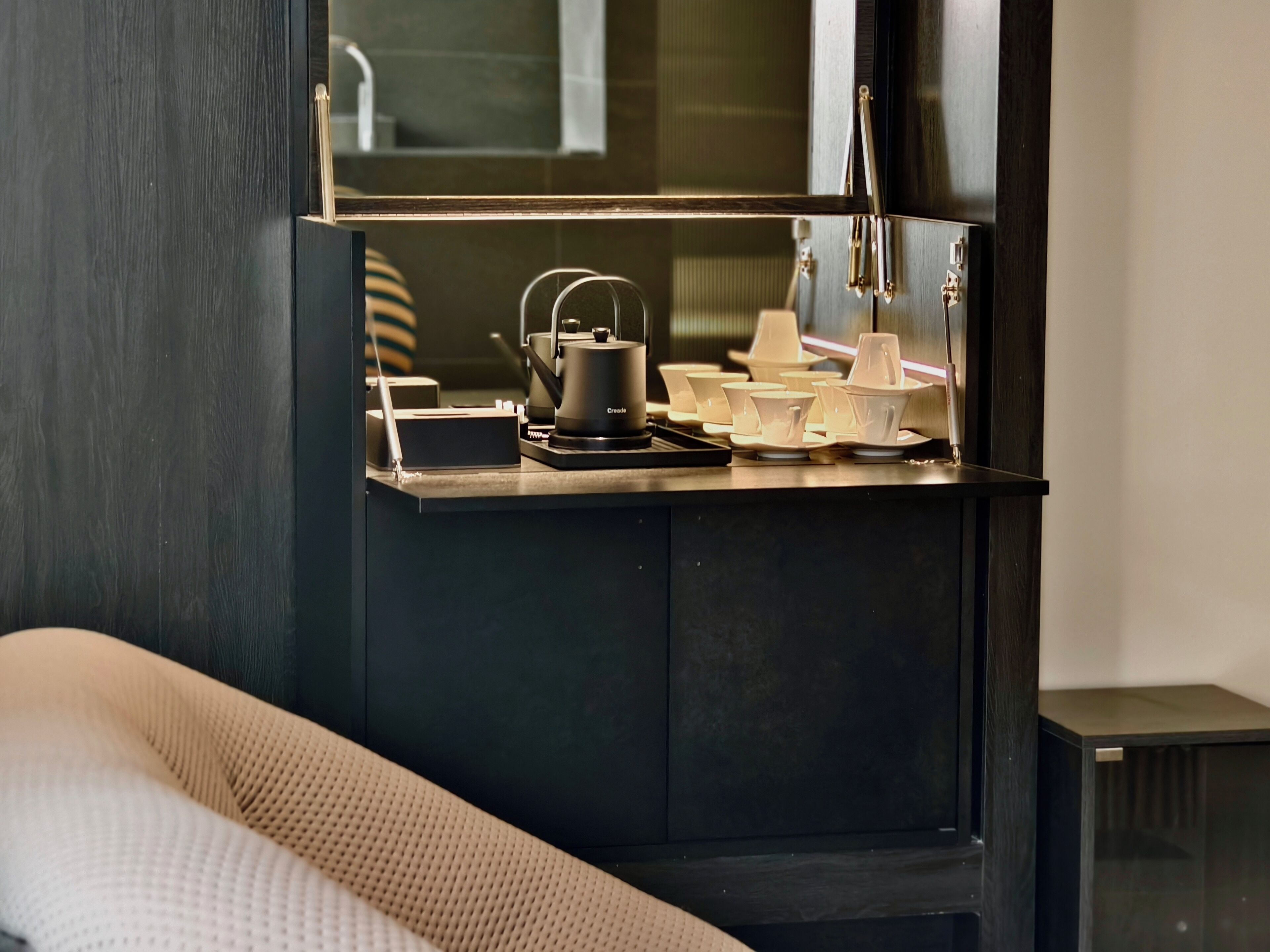 A kitchenette with a coffee maker, tea pot, and various cups and saucers.