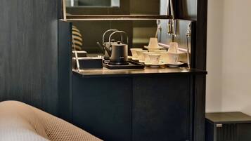 A kitchenette with a coffee maker, tea pot, and various cups and saucers.