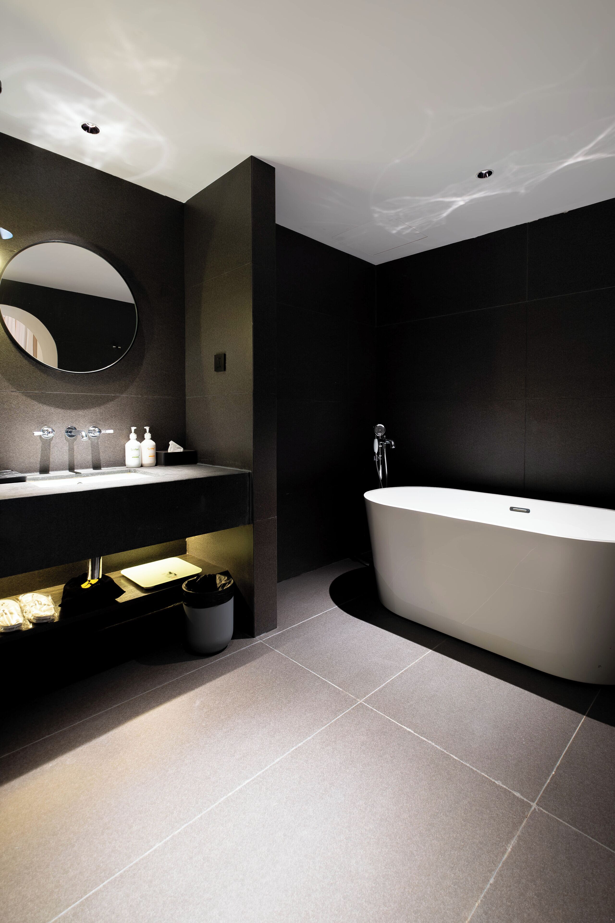 A modern bathroom with a large freestanding bathtub, a vanity with a mirror, and a trash bin.